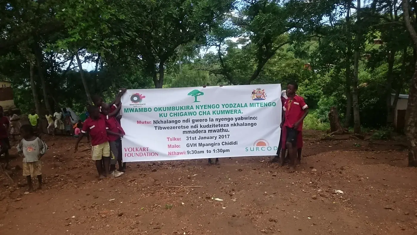 Community representatives gathered beside a banner for a tree-planting and forest-protection activity