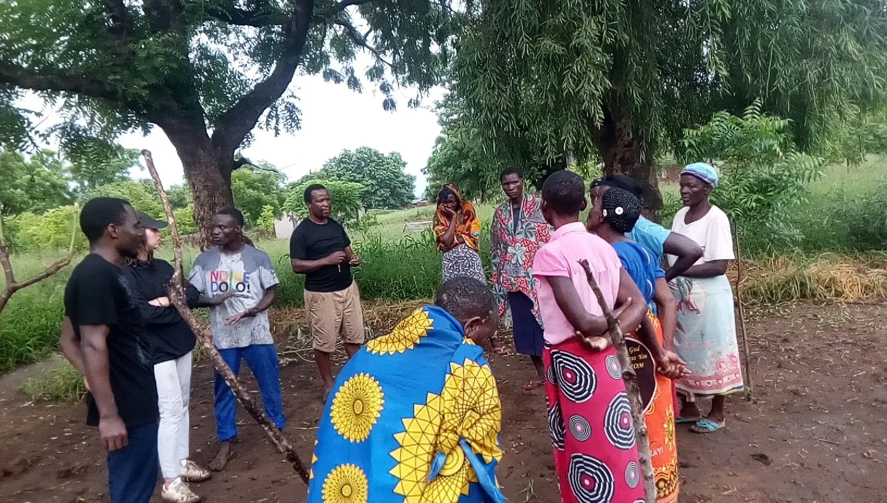 Community members and facilitators holding a group discussion in a cultivated field